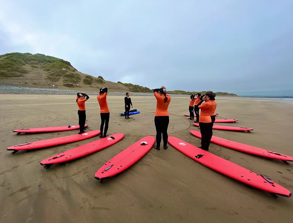 A surfing guide giving instructions to group of adult on a beach standing in circle