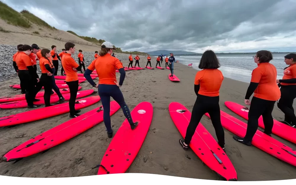 A surfing guide giving instructions to group of adult on a beach standing in circle